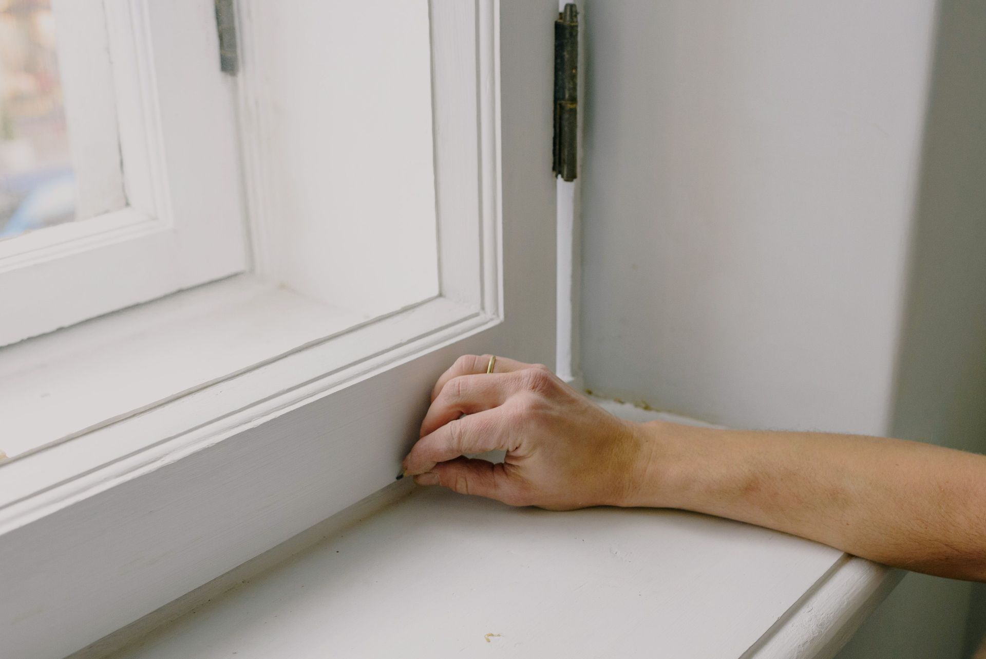 Side anonymous man putting arm on windowsill and touching white frame of window in daytime